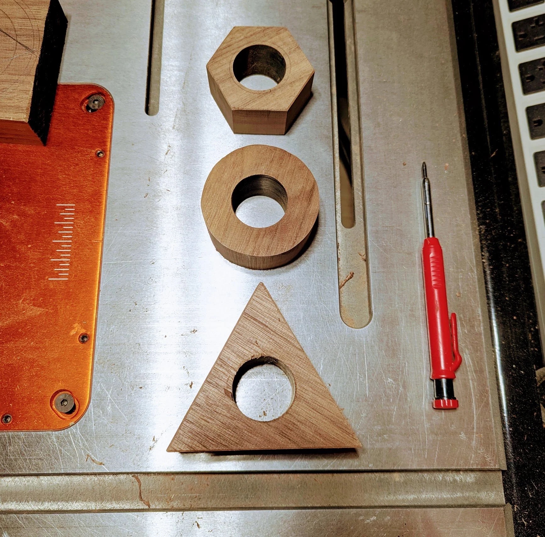 Three wooden nut prototypes — hexagon, circle, and triangle — on the table saw