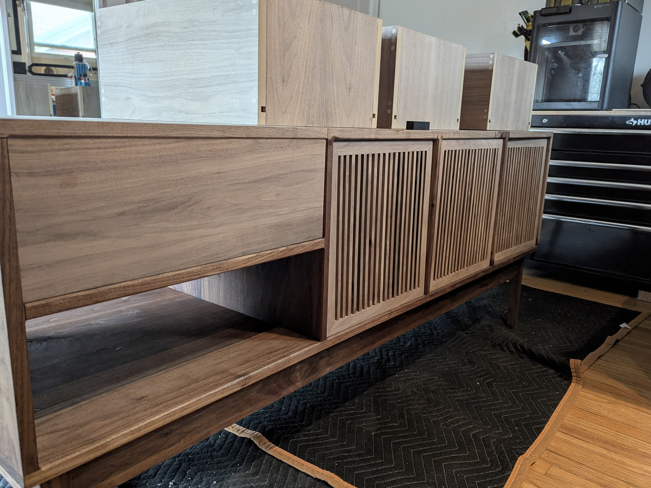 Dry fit in the shop — slatted doors hung, tapered legs under, the piece standing for the first time before finishing