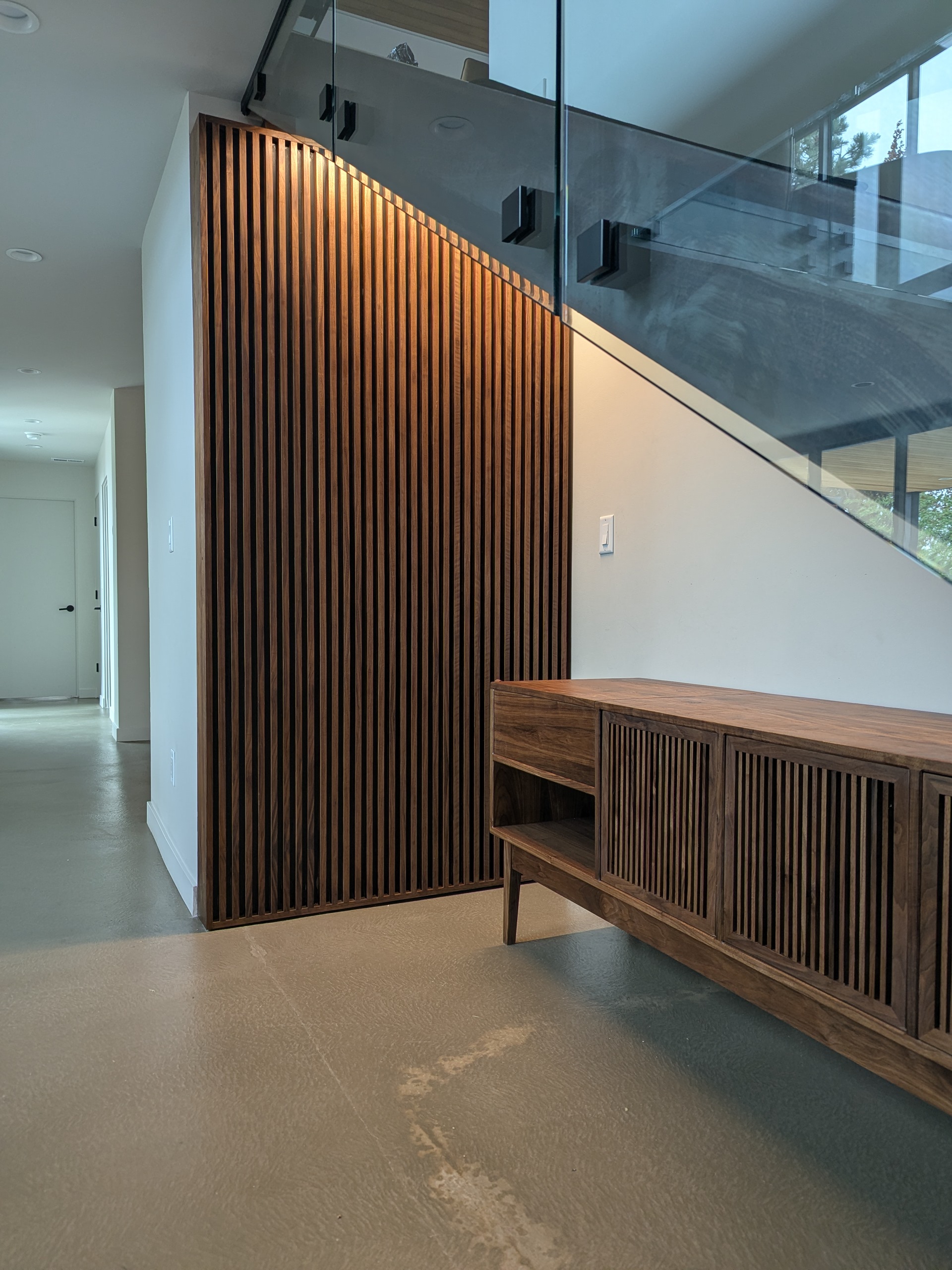 Tall portrait of The Nook's slatted wall panel backlit beside the credenza — same walnut, same slats, same DNA
