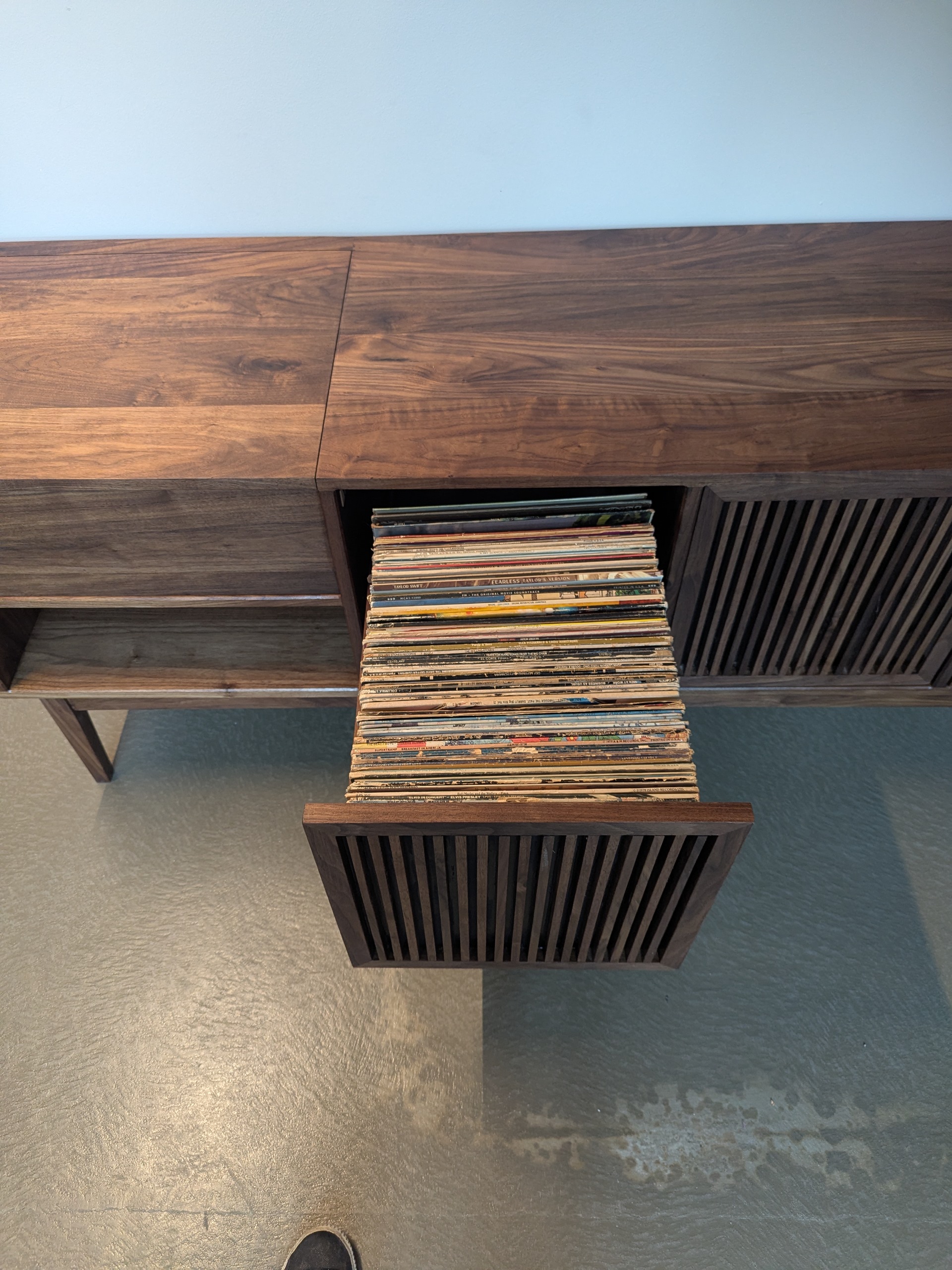 Top-down view of the credenza — walnut grain flowing across the top, one drawer pulled open with records stacked tight