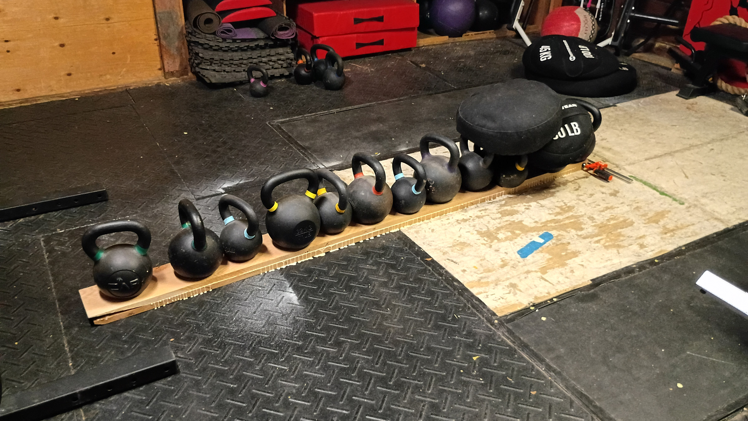 A row of kettlebells lined up on a white oak stile glue-up — improvised clamping in the shop-with-a-gym