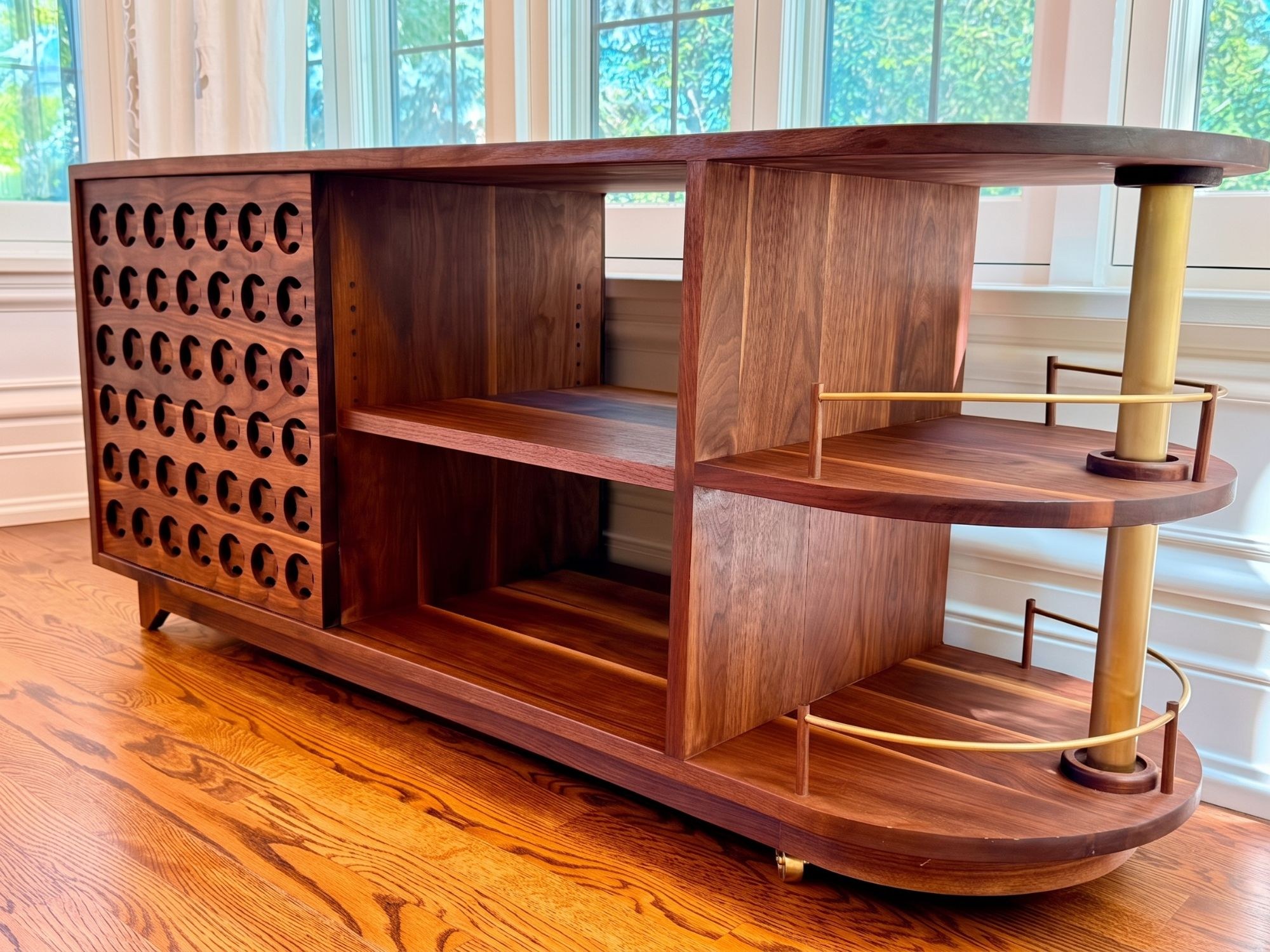 Brittney's Cart delivered: walnut buffet with the speaker-grille door, open shelving and curved brass rail, in her dining room by the windows