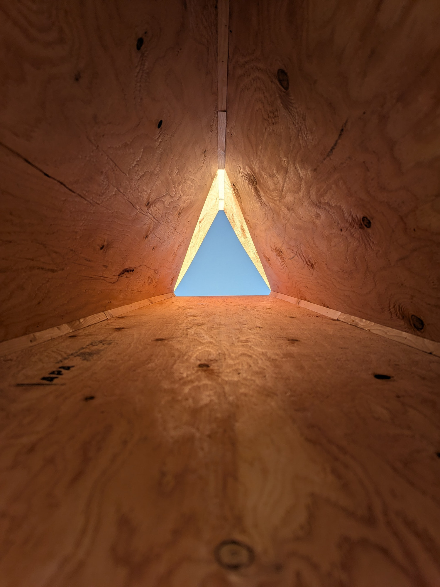 Looking up inside the plywood prototype: three walls converging on a small bright triangle of sky