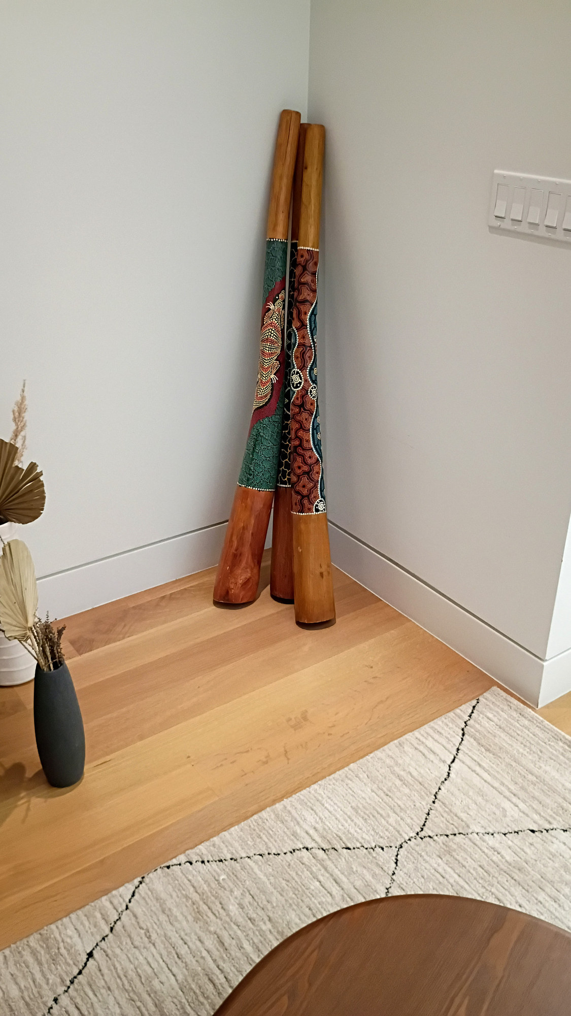 The three decorated didgeridoos leaning together in a corner of the living room