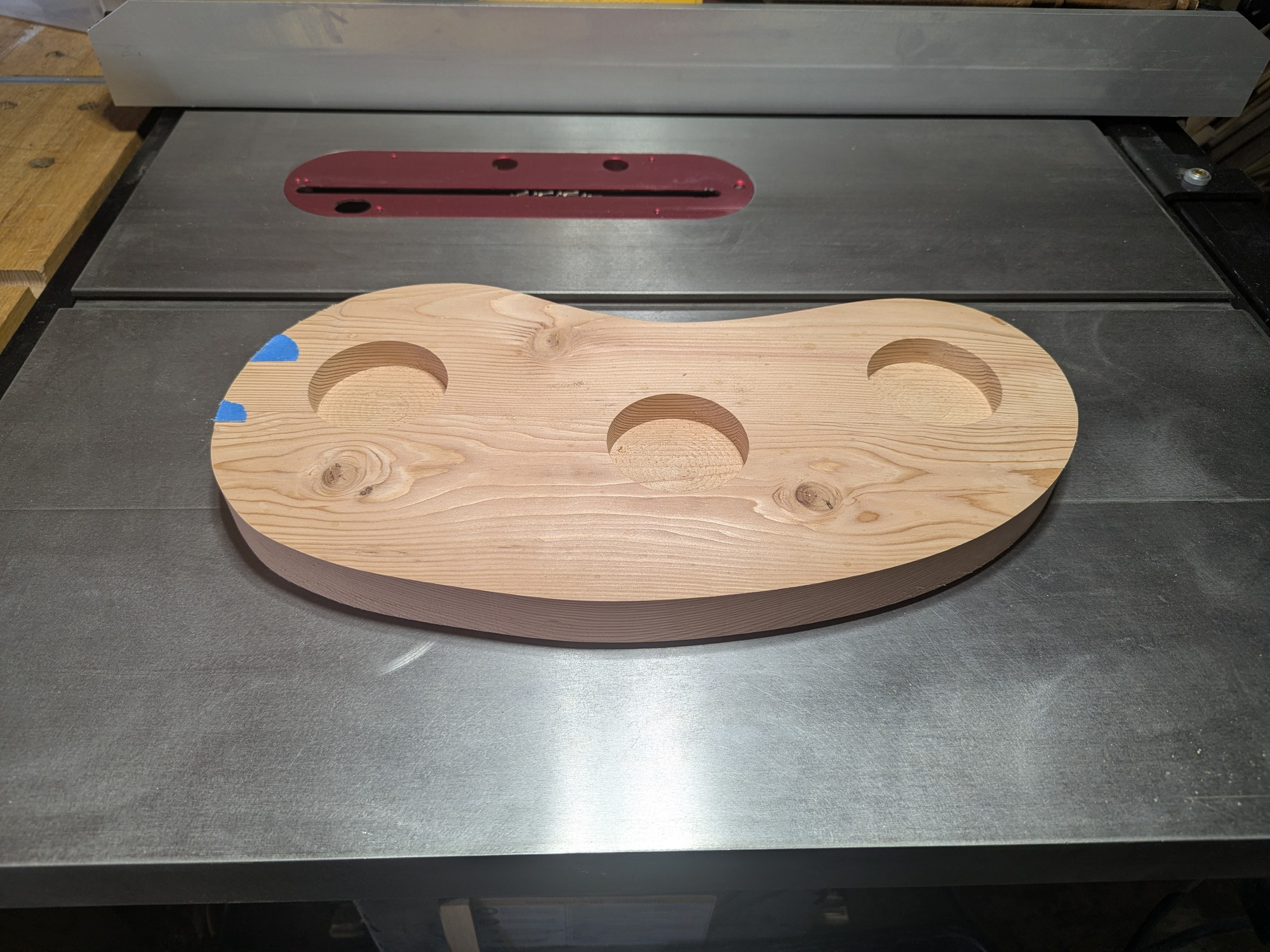 The softwood prototype of the bean-shaped base on the table saw, three bell seats bored through