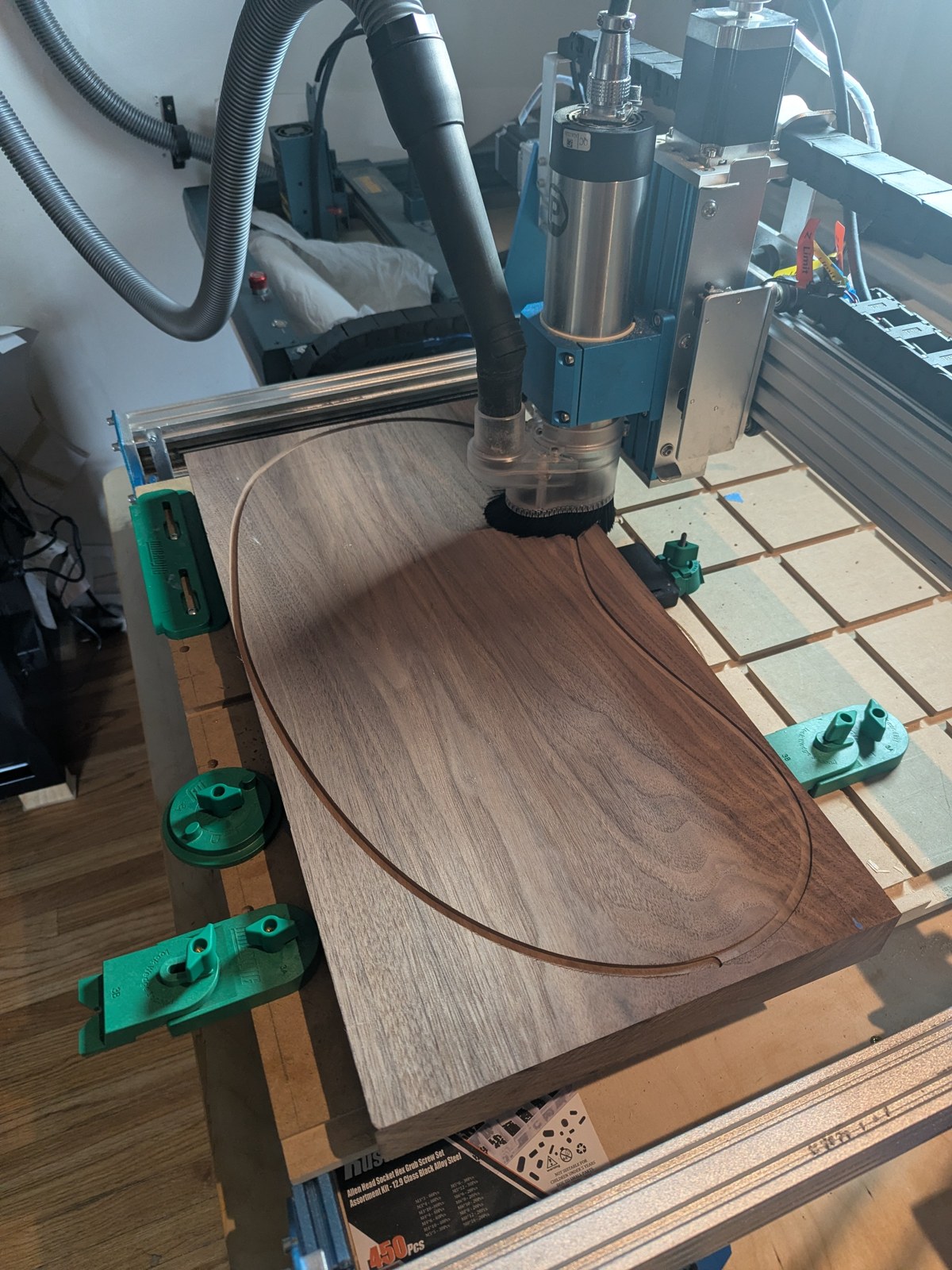The solid walnut slab clamped on the CNC, the bean outline cut through