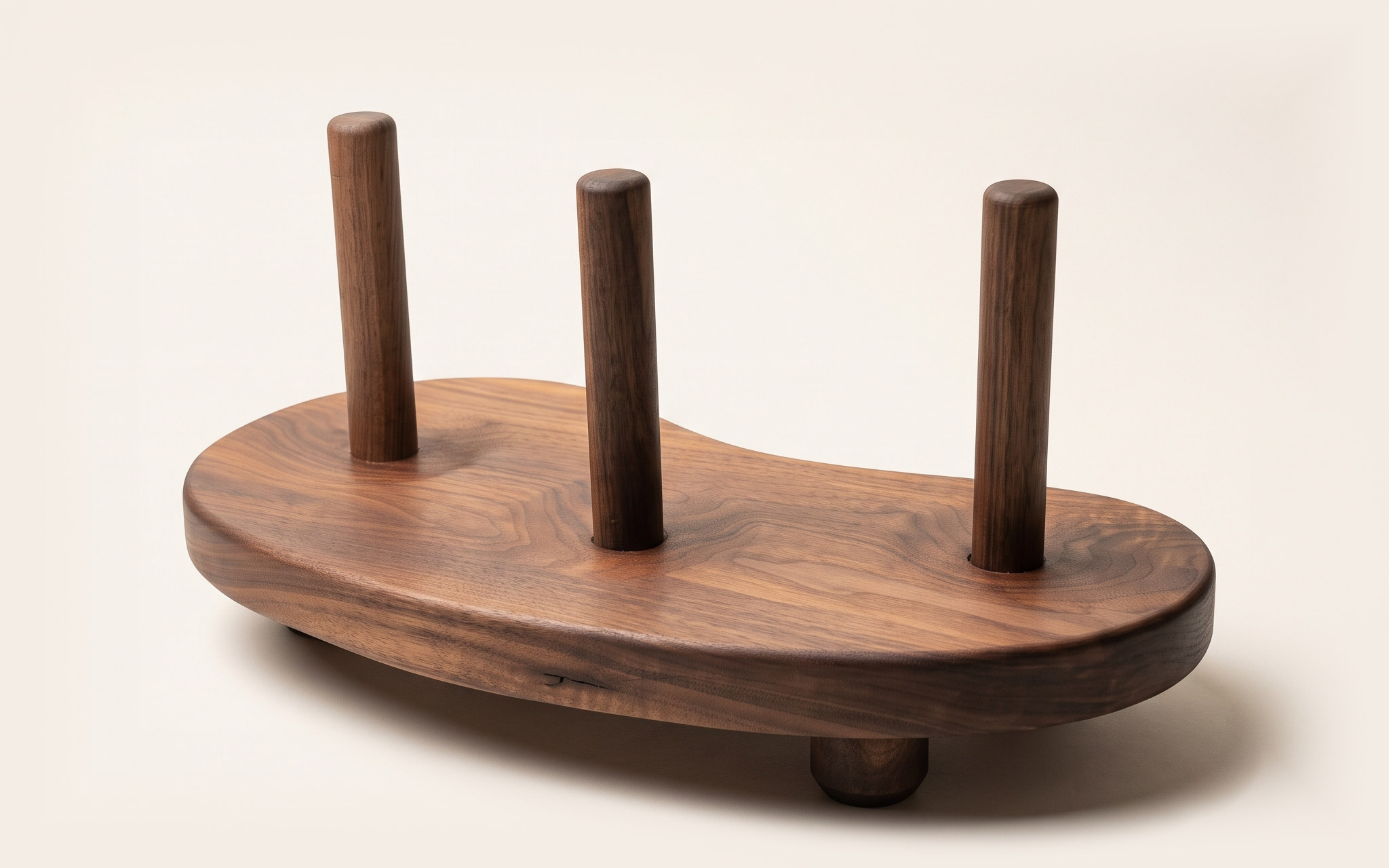 Yidaki: the finished stand, a bean-shaped slab of oiled black walnut with three turned walnut pegs rising from hand-carved recesses, on turned feet